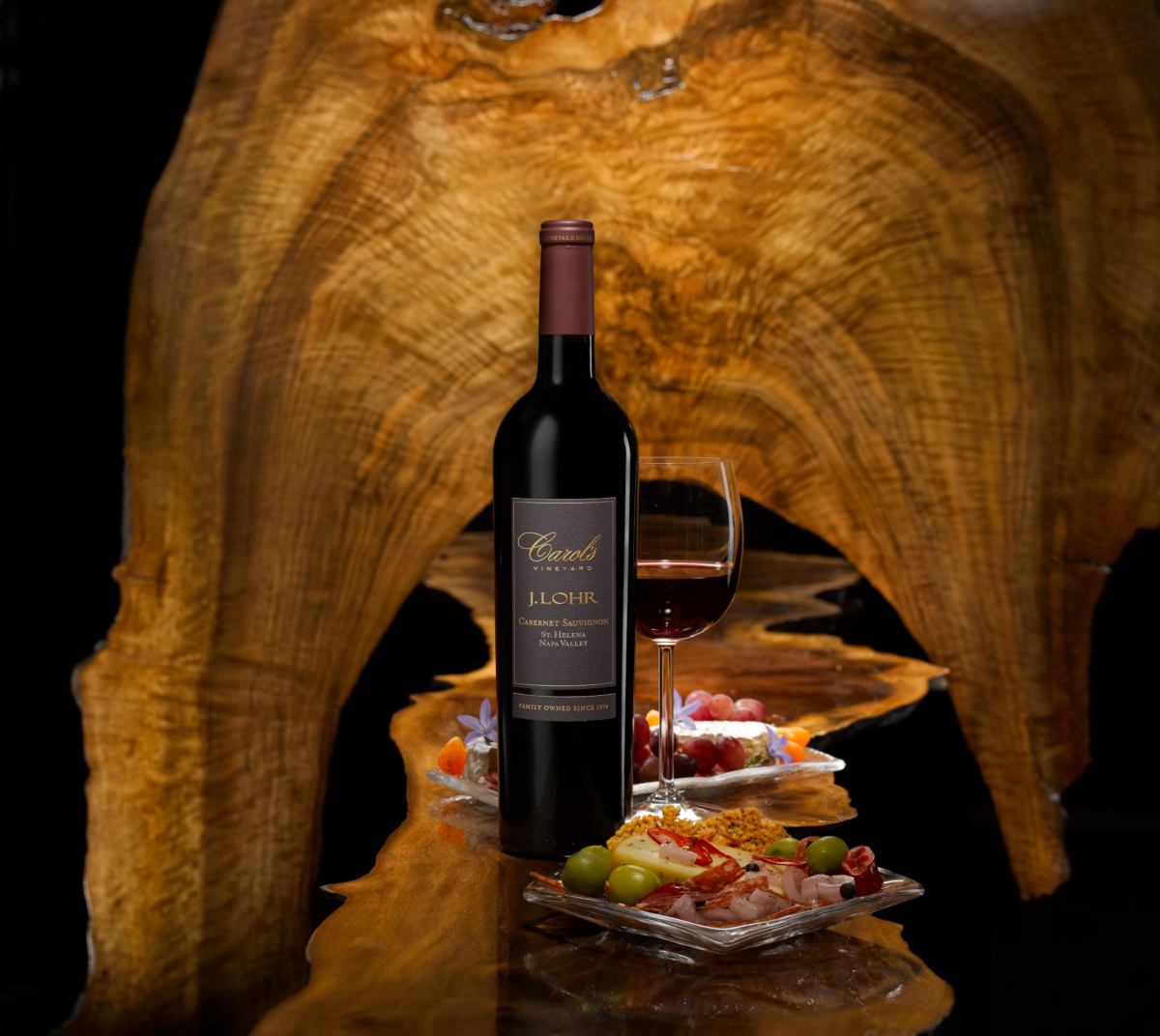 J. Lohr Carol's Vineyard Cabernet and plates of appetizers with a dark wood background